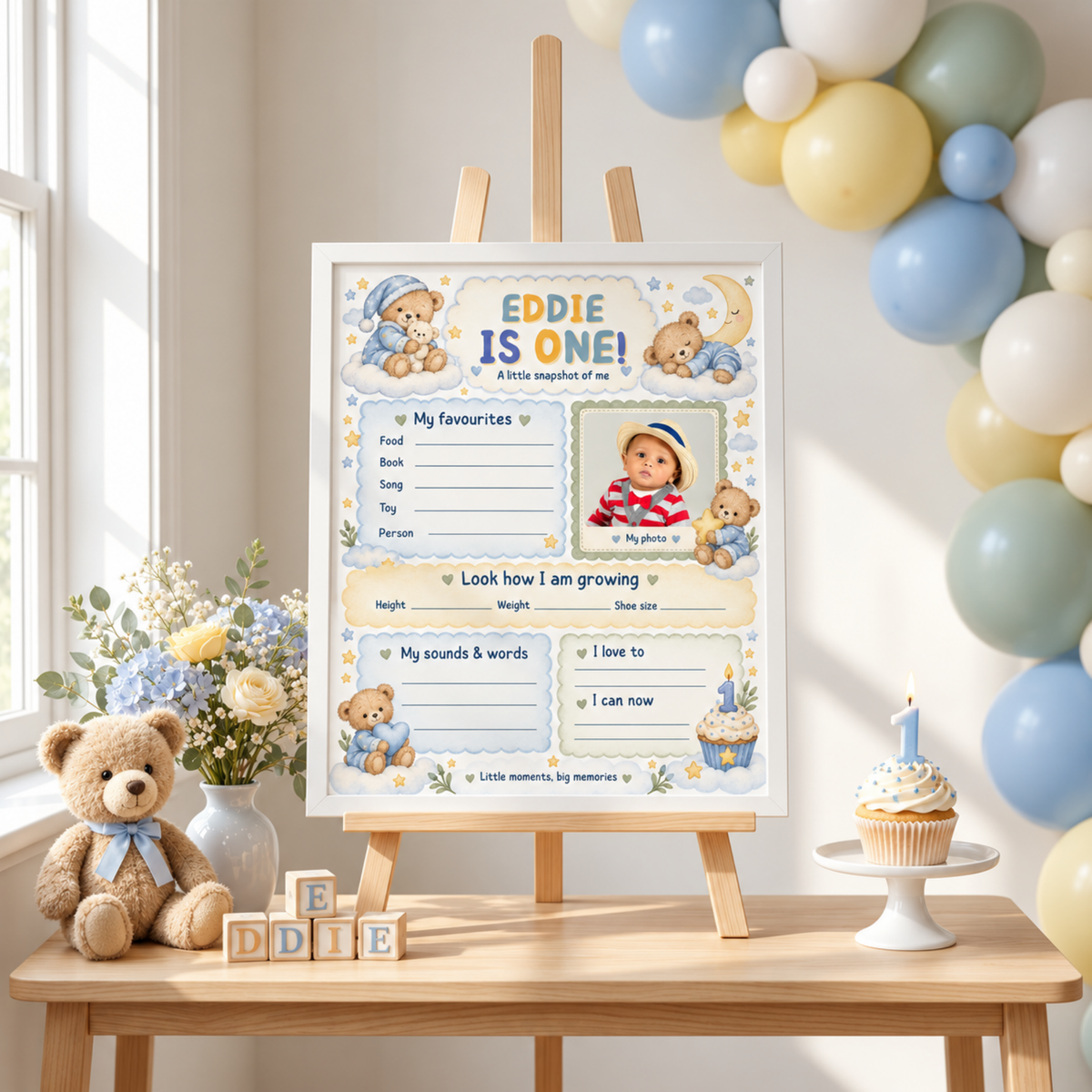 Boy's teddy bear first birthday milestone poster with a photo area and blue memory sections, framed on a tabletop easel.